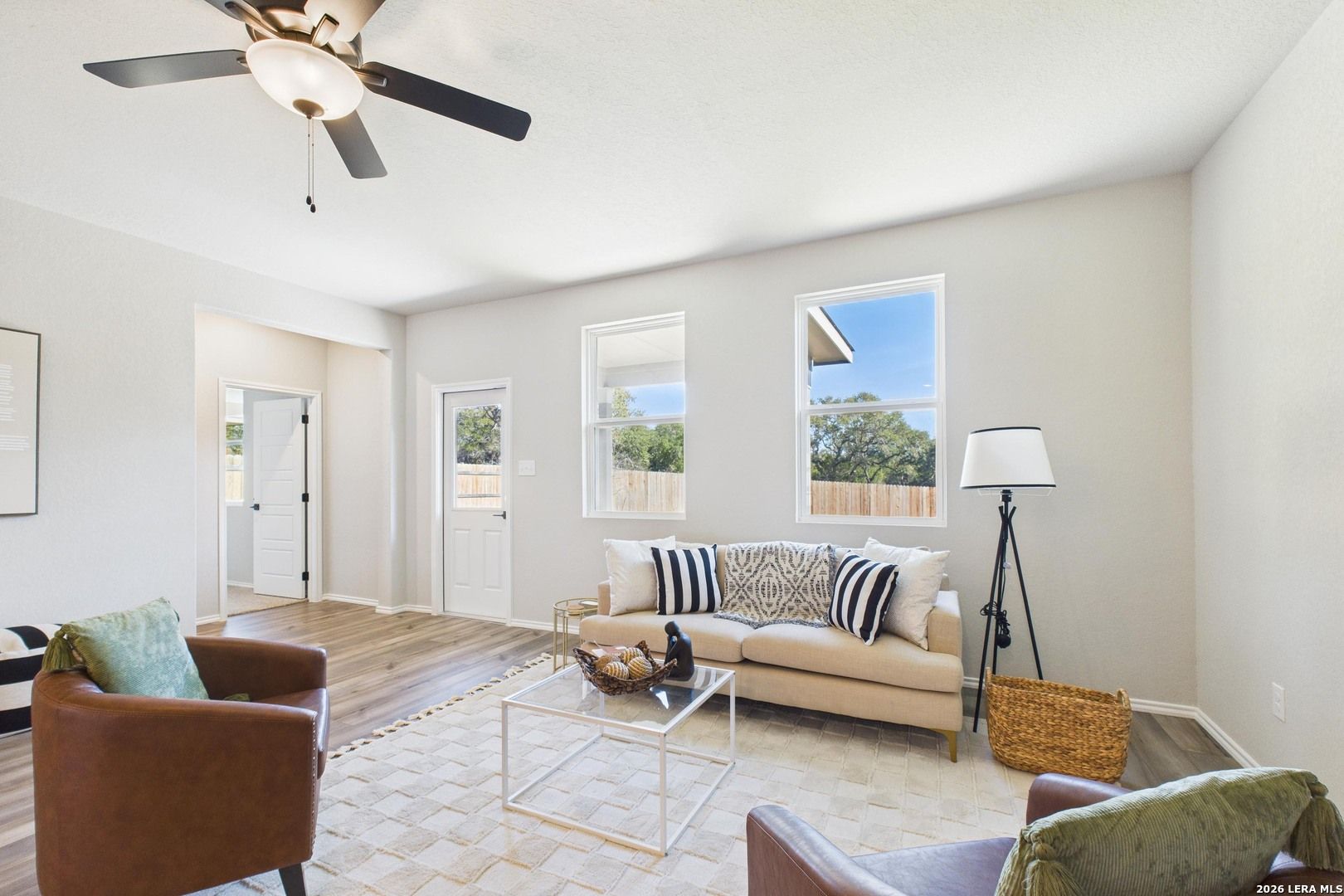Cozy living room with beige sofa, leather armchairs, ceiling fan, large windows in Davidson Homes The Douglas E, Bricewood, San Antonio