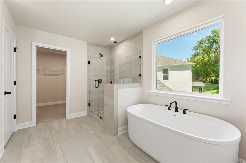 Elegant master bathroom with freestanding soaking tub, frameless glass shower, and garden view in Davidson Homes The Hickory E, Buford, GA