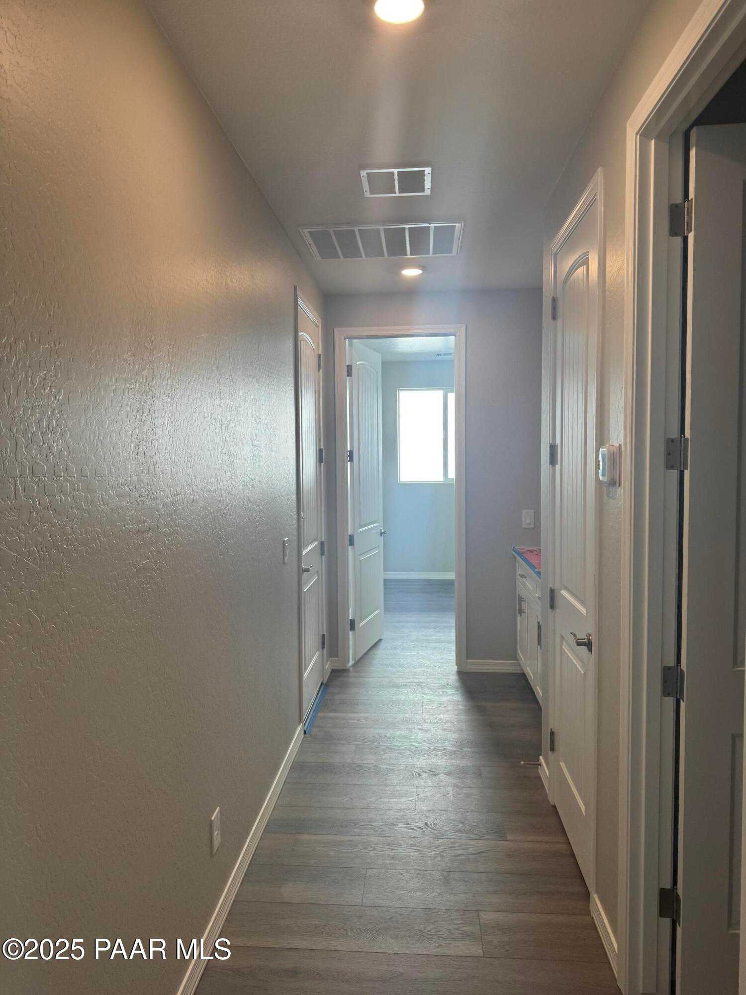 Bright hallway with beige walls, hardwood floors, white doors, and recessed lighting in Davidson Homes The Monarch E, Prescott, Arizona