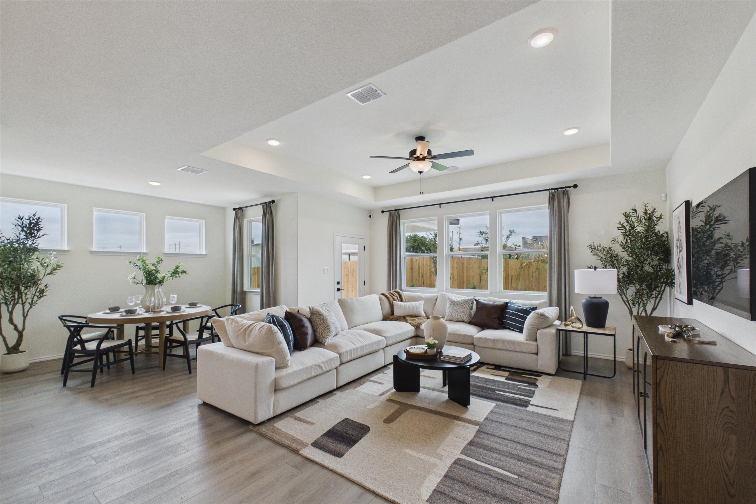 Open-concept living and dining room in Rayburn Valley San Antonio home by Davidson Homes featuring white sectional sofa, oval table, and large windows