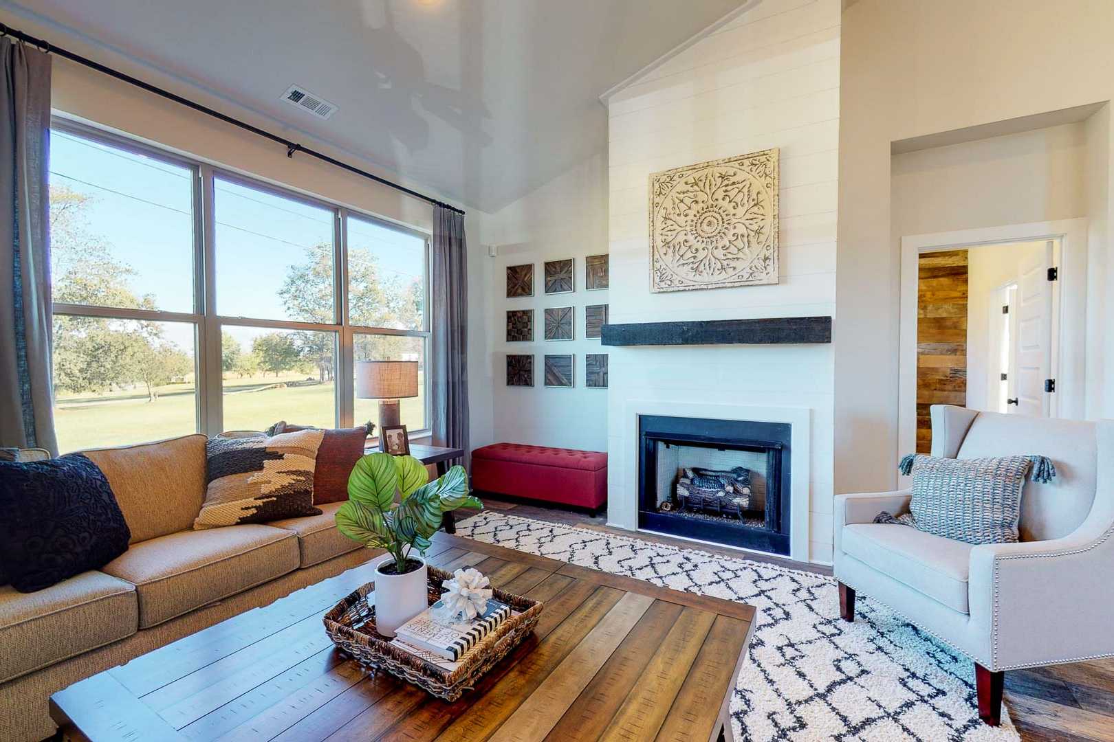 Cozy living room at Liberty Creek in Gallatin TN with gas fireplace, large windows overlooking fields, beige sofa, armchair, and modern decor
