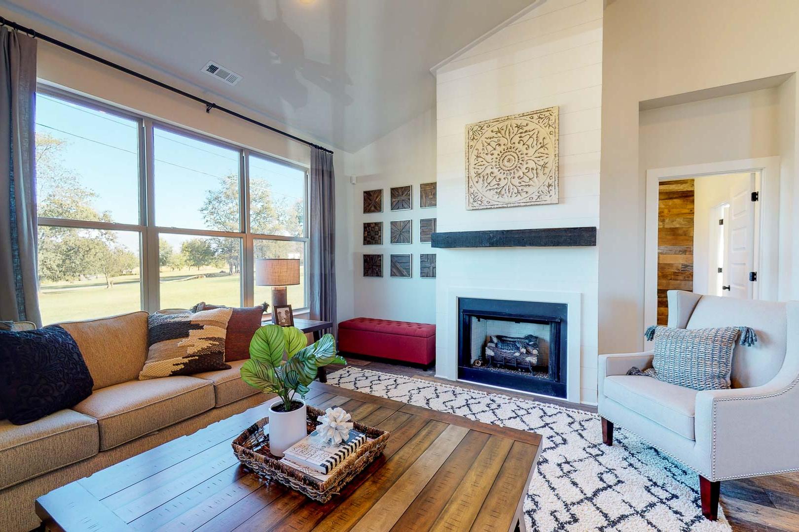 Cozy living room at Liberty Creek in Gallatin TN with gas fireplace, large windows overlooking fields, beige sofa, armchair, and modern decor