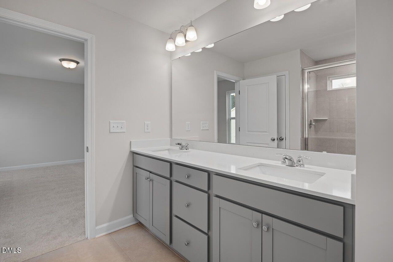 Modern master bathroom with double vanity, gray cabinets, white quartz counters, and glass shower in The Gavin B, Lillington, NC