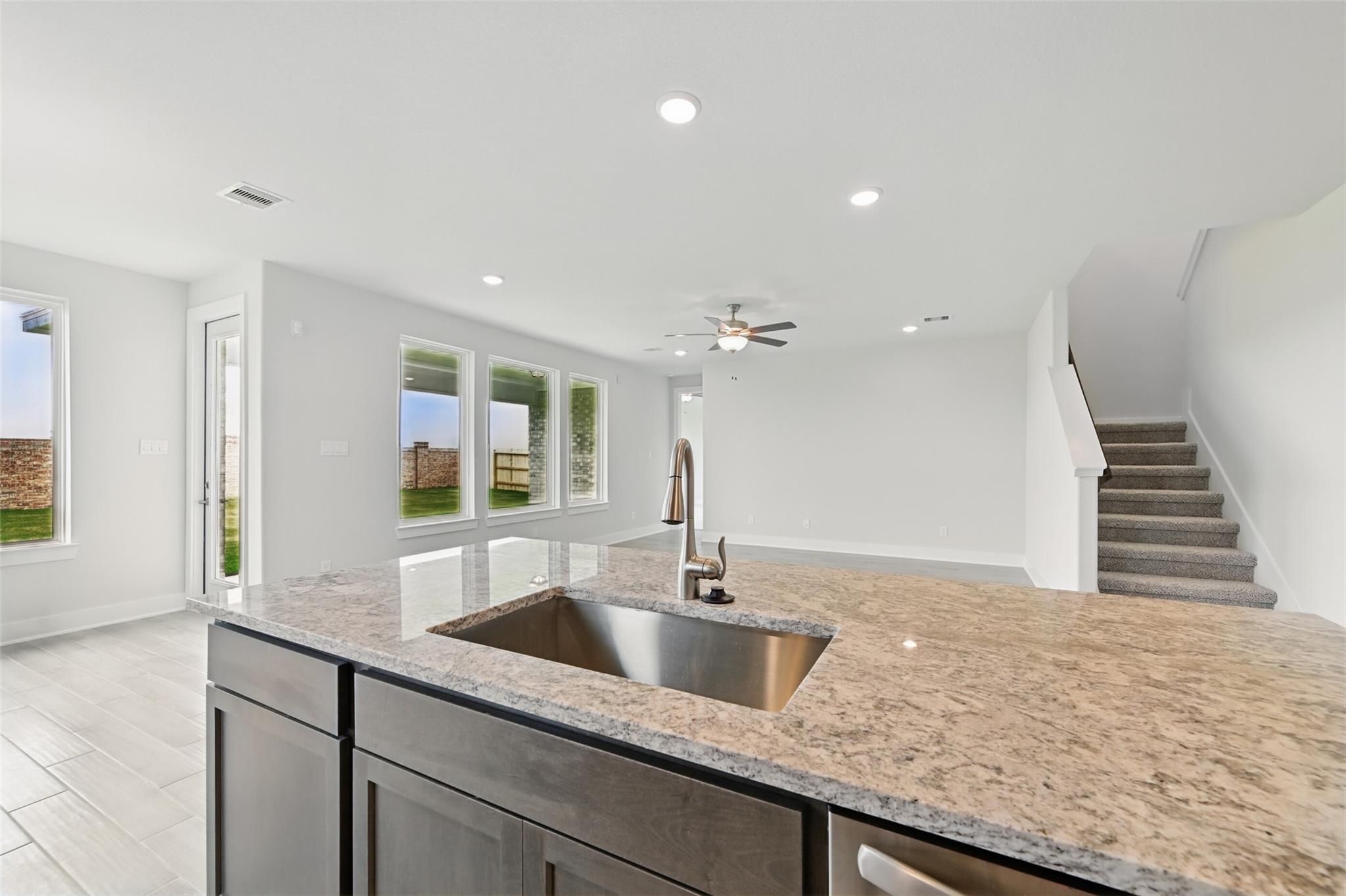 Modern open-concept kitchen with granite island, stainless sink, and ceiling fan in Davidson Homes The Philip A, Lago Mar