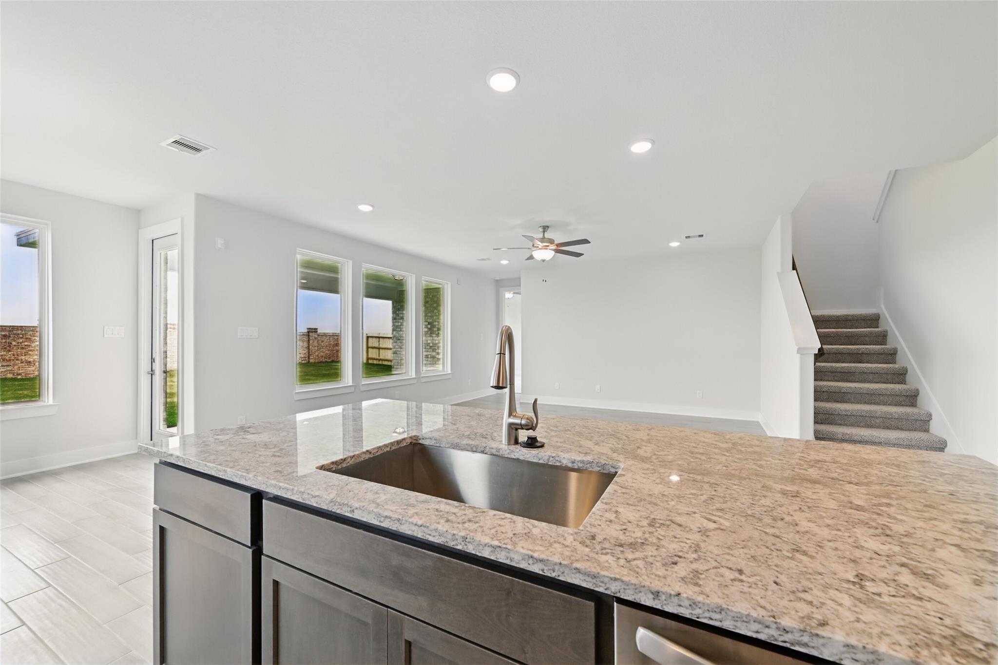 Modern open-concept kitchen with granite island, stainless sink, and ceiling fan in Davidson Homes The Philip A, Lago Mar