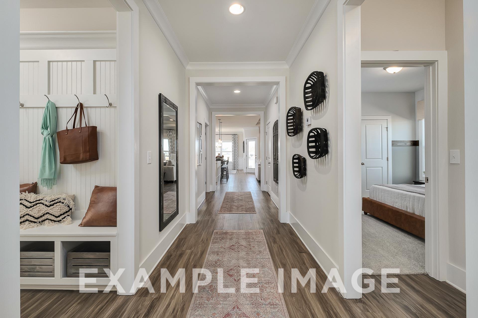 Spacious hallway in The Everett home design by Davidson Homes with white walls, wood floors, runner rug, coat hooks, and mirror