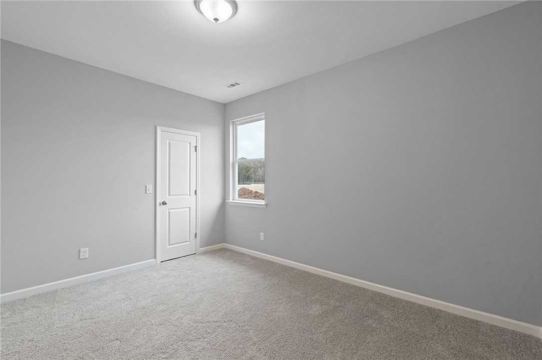 Modern empty bedroom featuring gray walls, plush carpet, white door, and window view in Davidson Homes The Luna B, Opelika, Alabama