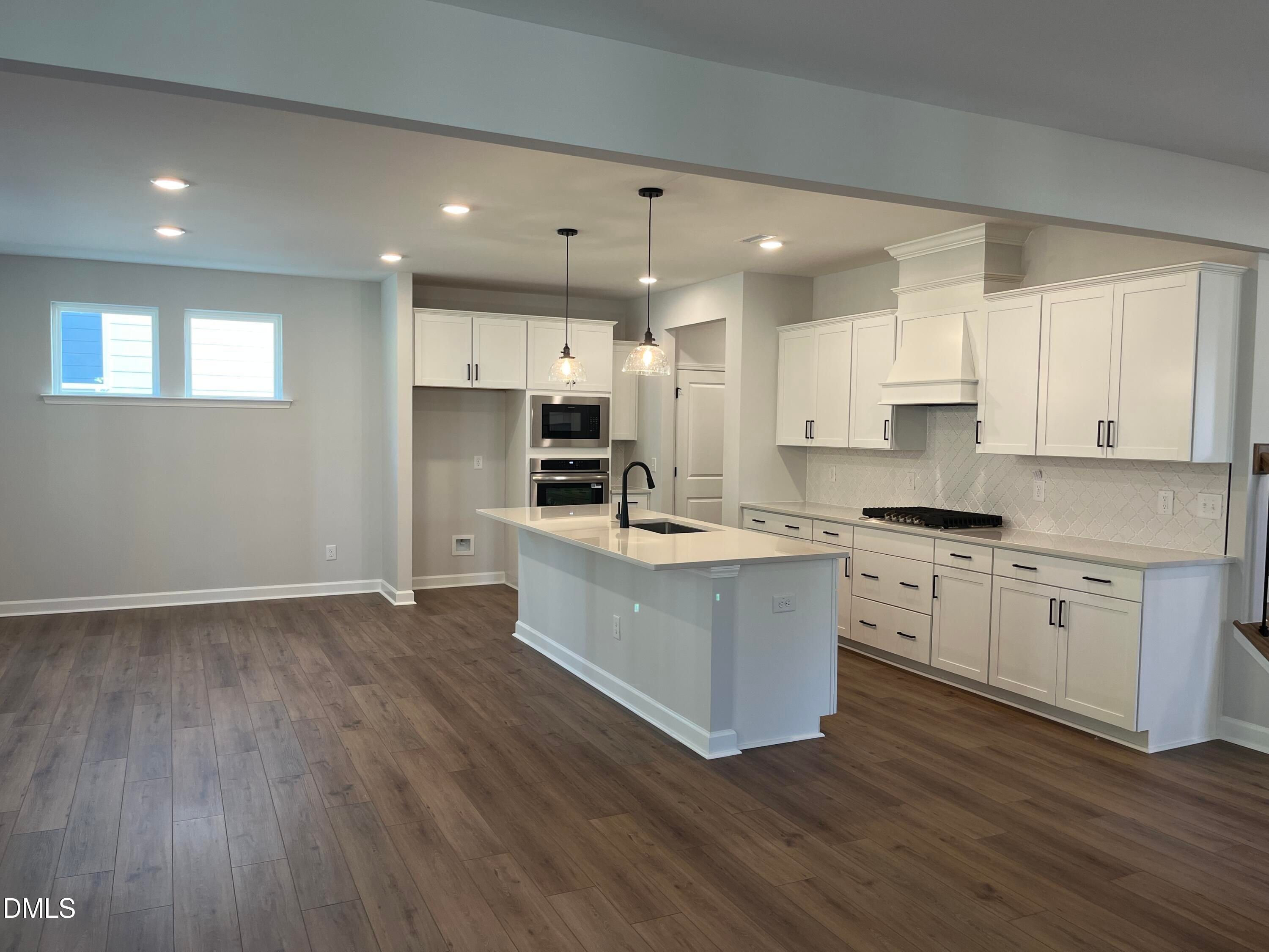 White kitchen with island, pendant lights, and hardwood-style floors in Davidson Homes The Beech C, Sage on North Main, Wake Forest, NC