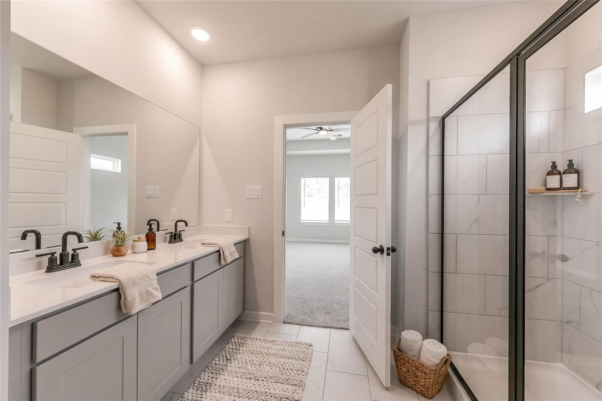 Modern master bathroom featuring double vanity with gray cabinets, black faucets, and frameless glass shower in Davidson Homes The Everett C, Crosby, Texas