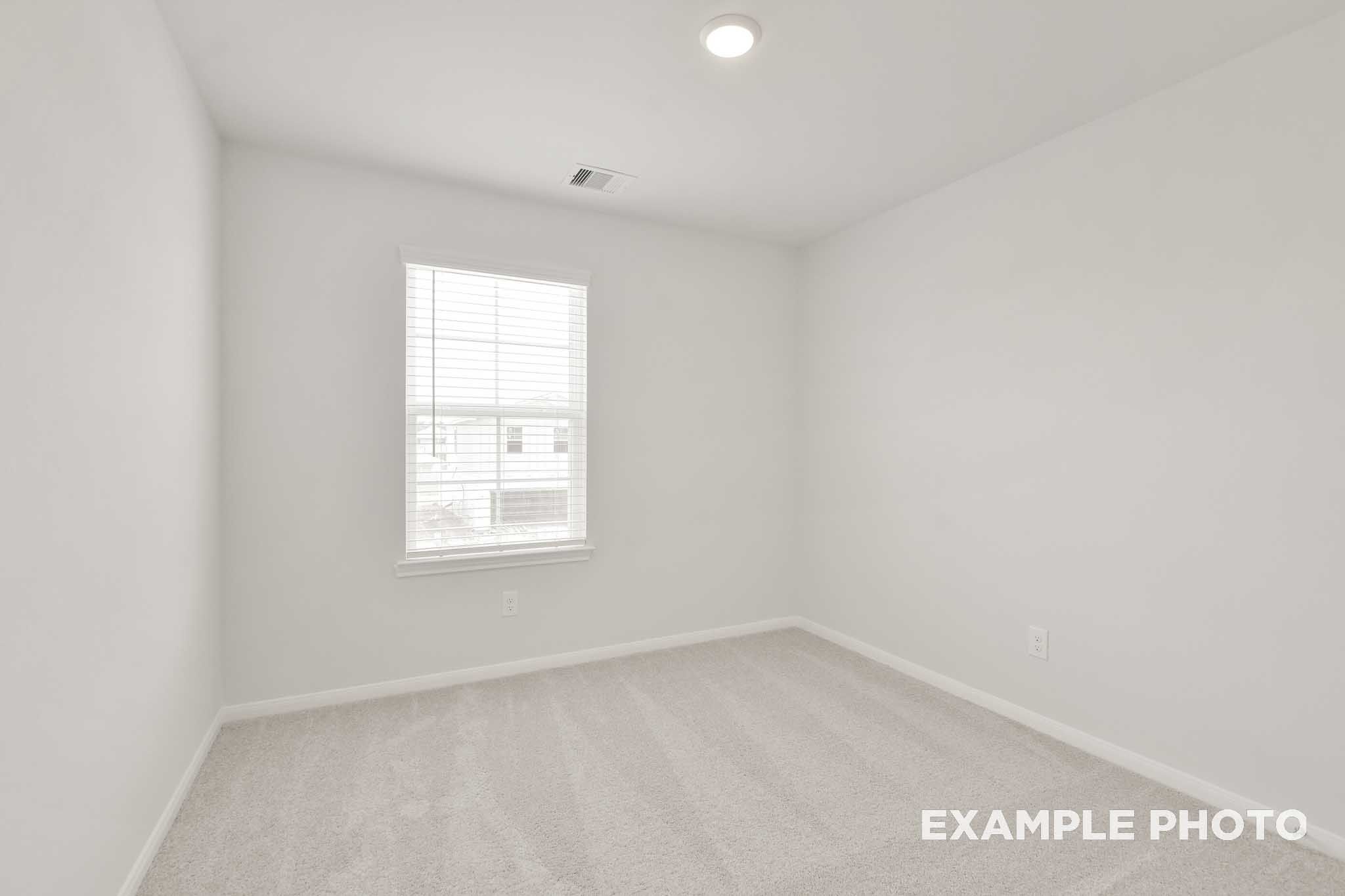 Bright empty bedroom with white walls, carpet flooring, and window with blinds in The Brazos by Davidson Homes, Beasley TX