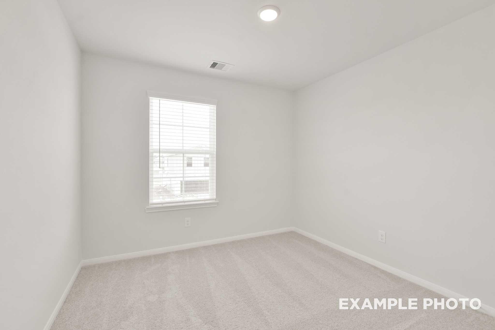 Bright empty bedroom with white walls, carpet flooring, and window with blinds in The Brazos by Davidson Homes, Beasley TX