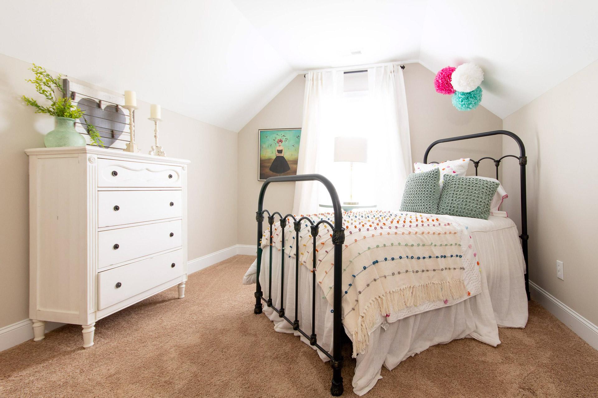 Cozy attic bedroom at Summer Pointe in Madison Alabama with black iron bed colorful quilt white dresser and sloped ceiling