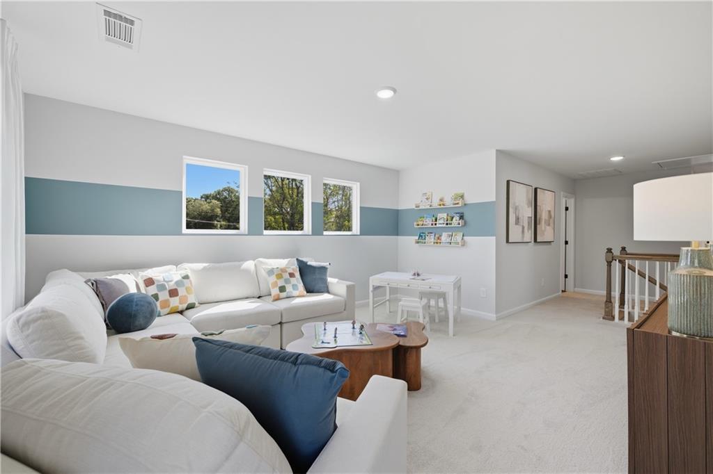 Bright upstairs bonus room with white sectional, blue accent wall, and kids' play area in The Sinclair B, Greene Farm, Cartersville, GA