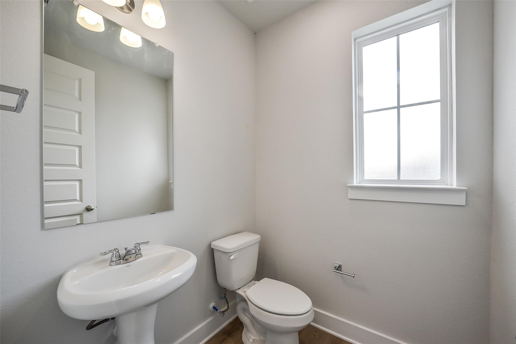 Bright powder room with pedestal sink, white toilet, large mirror, and window in Davidson Homes The Philip B, Rosharon, Texas