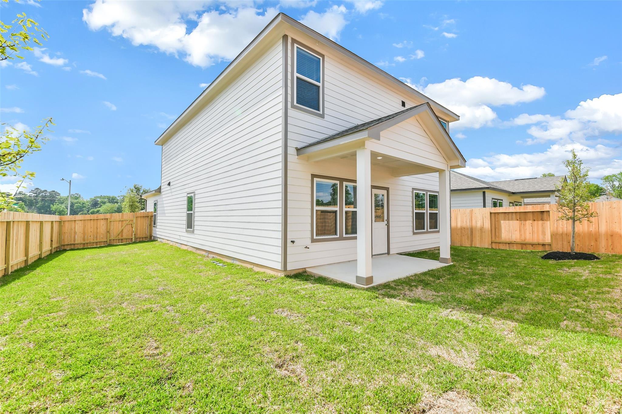 Two-story white home with covered back patio, glass doors, fenced green lawn, and young trees in Conroe, Texas