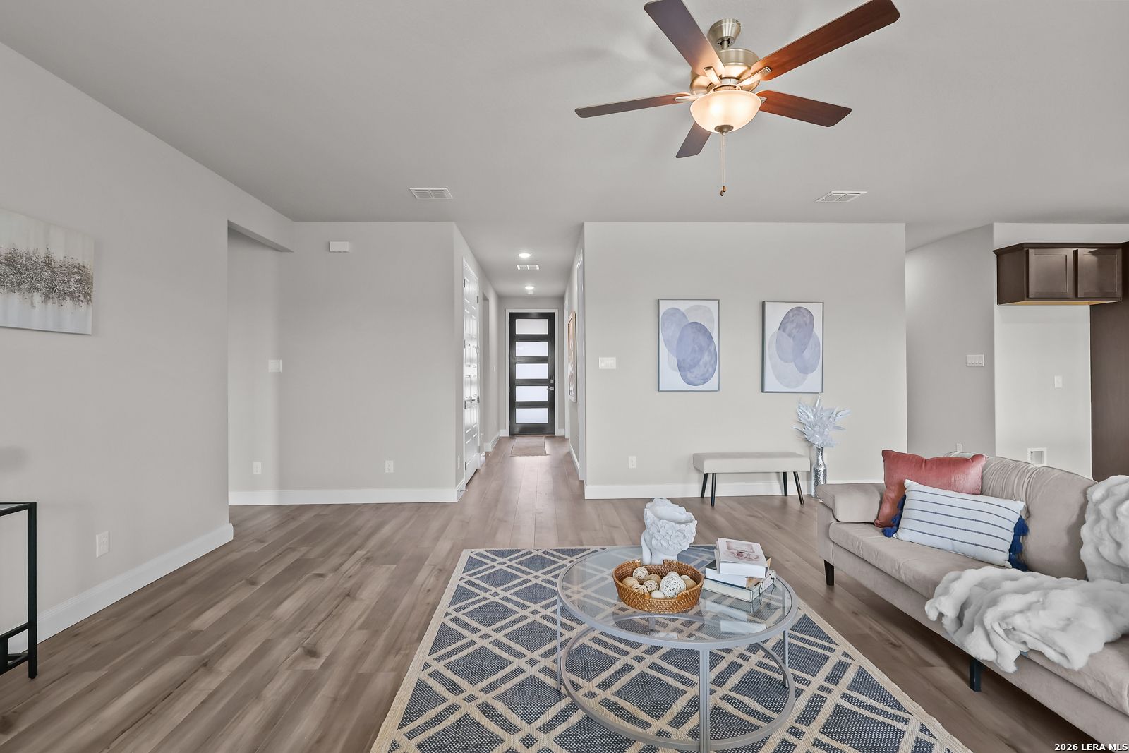 Cozy living room with hardwood floors, beige sofa, glass coffee table, and abstract art in Davidson Homes The Rockford G, Ladera, San Antonio