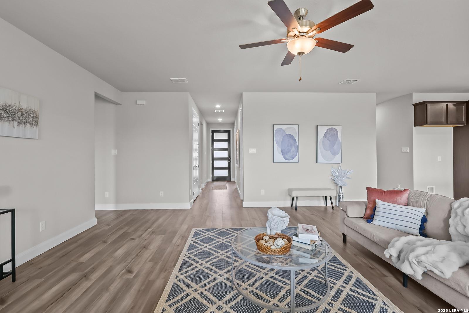 Cozy living room with hardwood floors, beige sofa, glass coffee table, and abstract art in Davidson Homes The Rockford G, Ladera, San Antonio