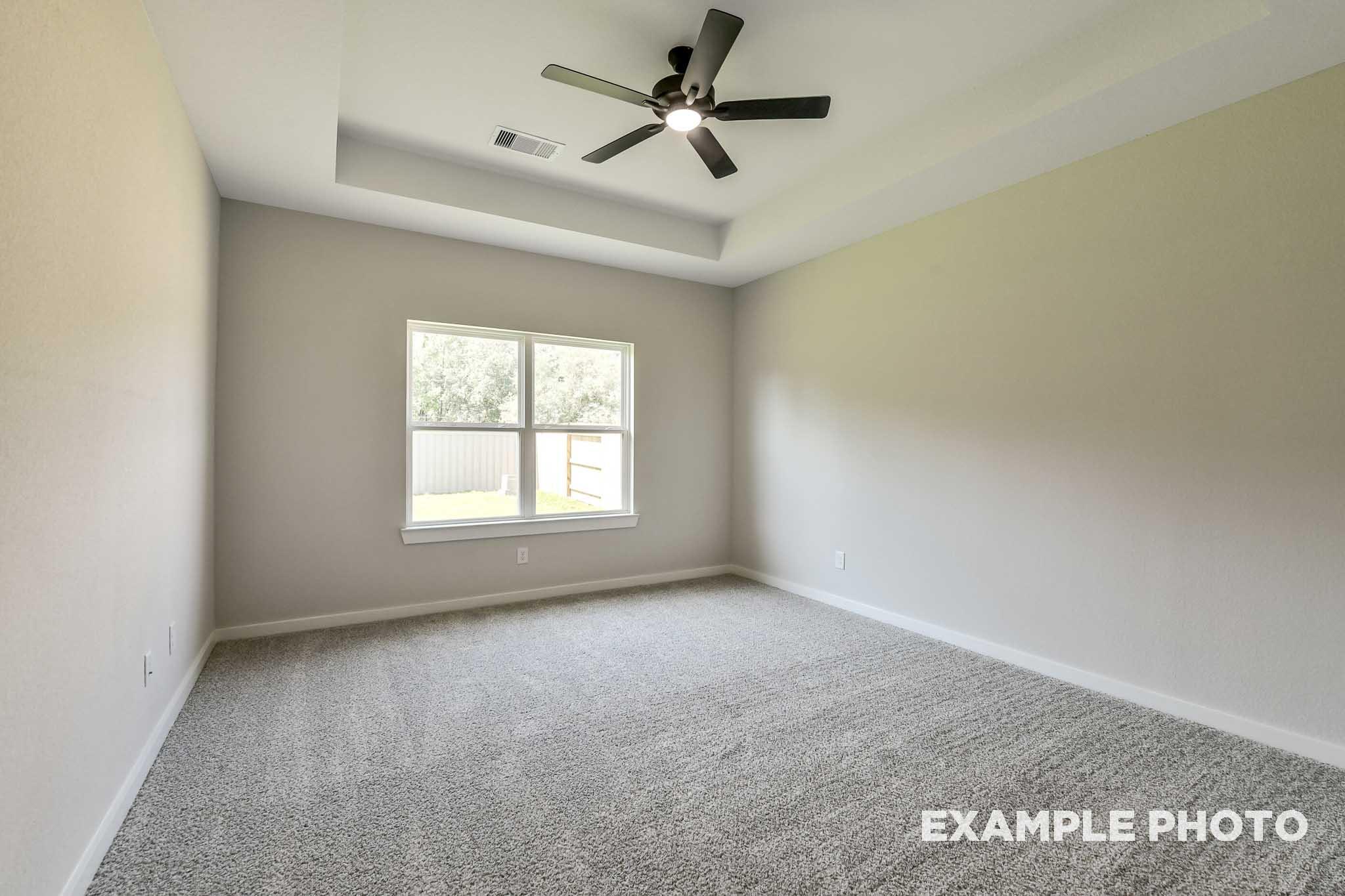 Spacious secondary bedroom in The Daphne G with neutral beige walls, gray carpet, dual ceiling fans, and large window to backyard