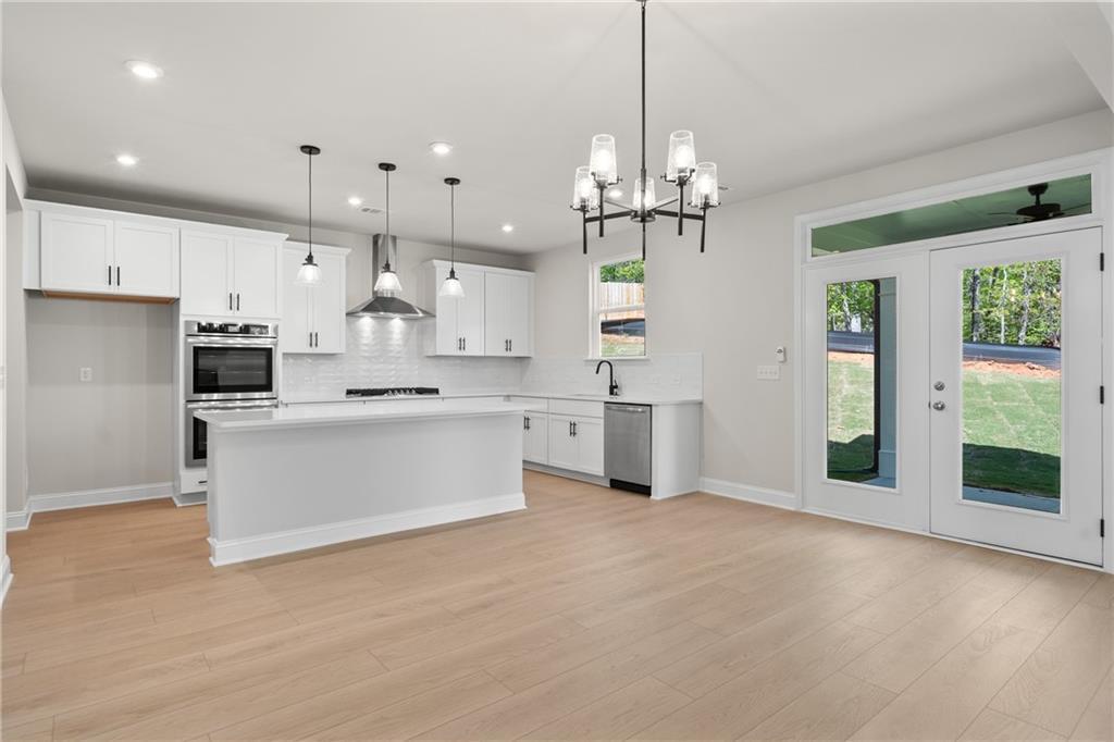 Open-concept kitchen with white cabinets, large island, stainless appliances, and French doors to lush backyard in The Hickory E, Buford, GA
