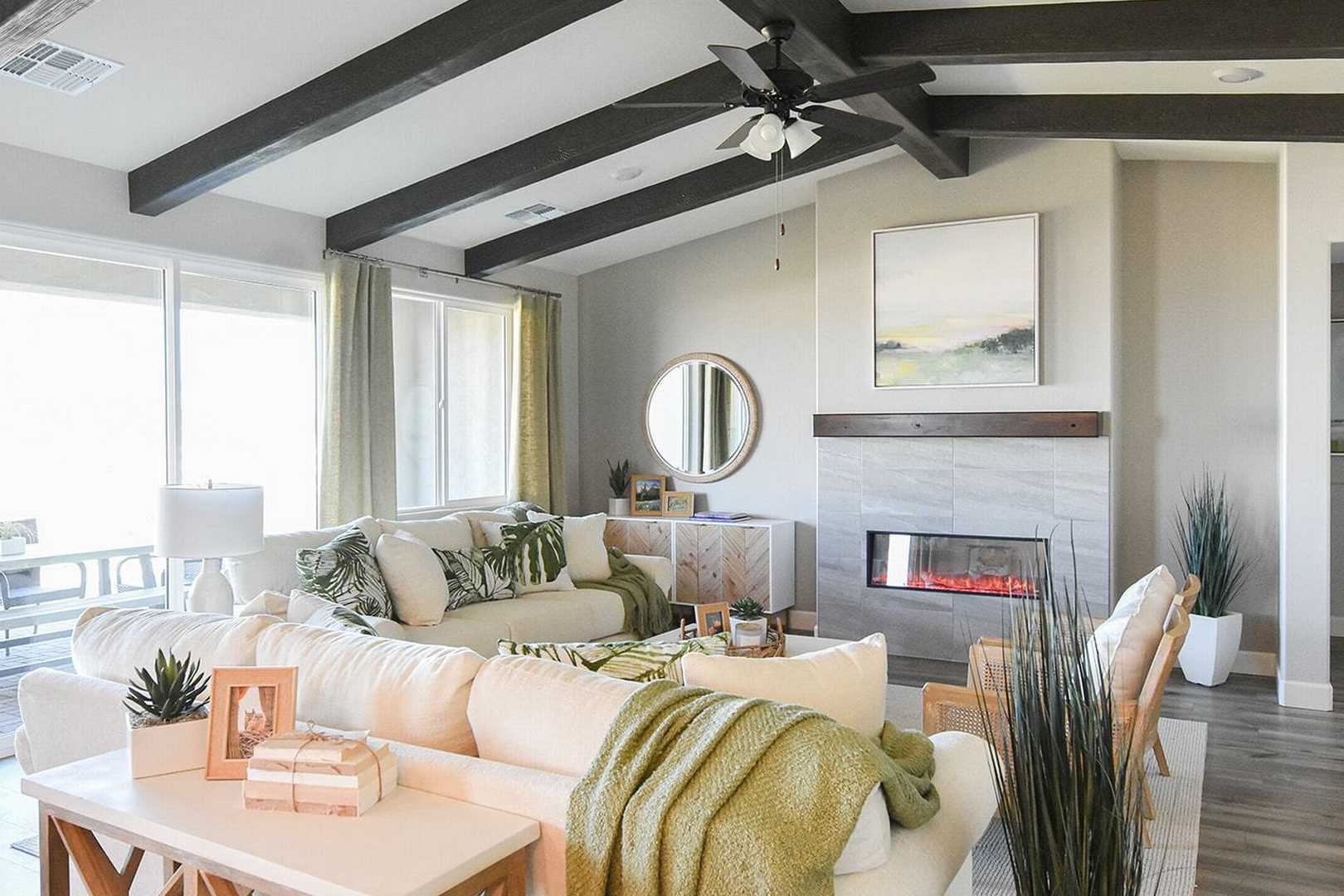 Spacious living room in The Summit B by Evermore Homes featuring white sectional sofa, modern gas fireplace, wooden ceiling beams, and large windows in Prescott Valley home
