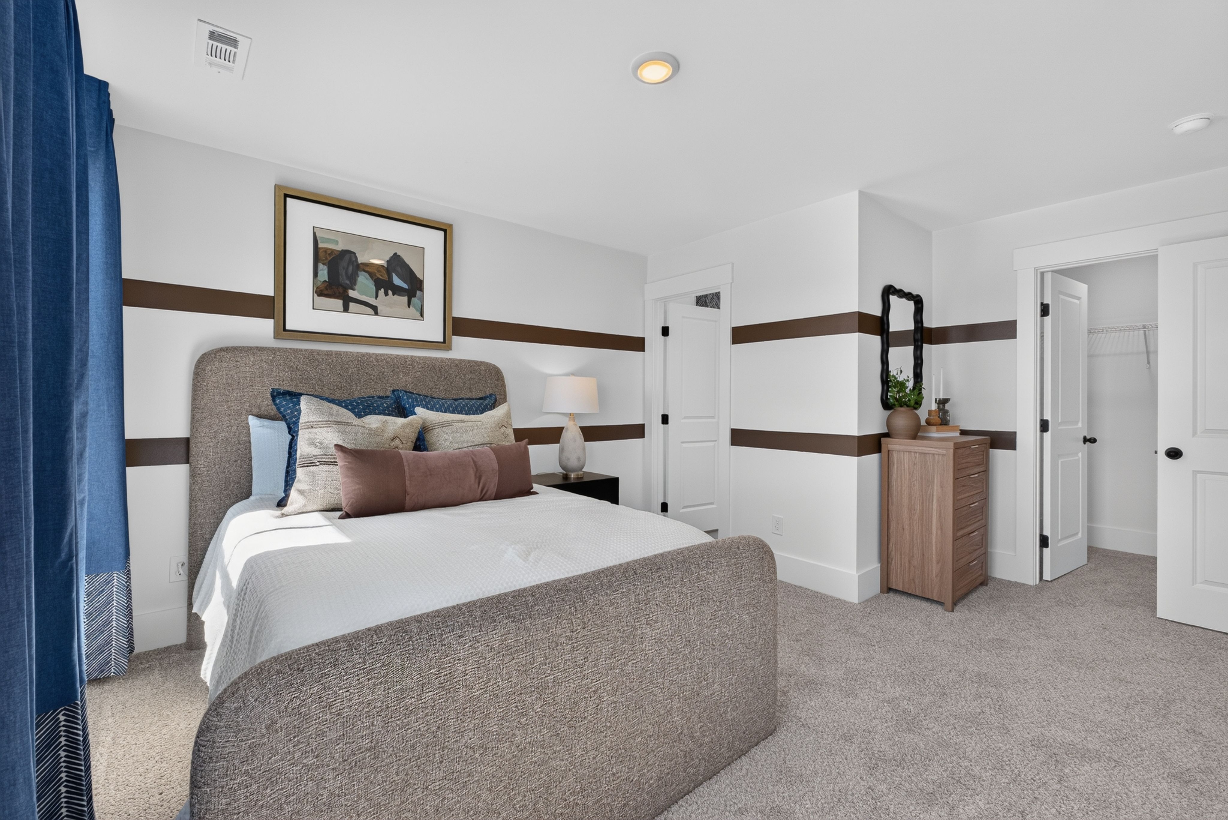 Upholstered bed in primary bedroom at Evergreen Mill in Madison, AL by Davidson Homes with striped accent walls and walk-in closet