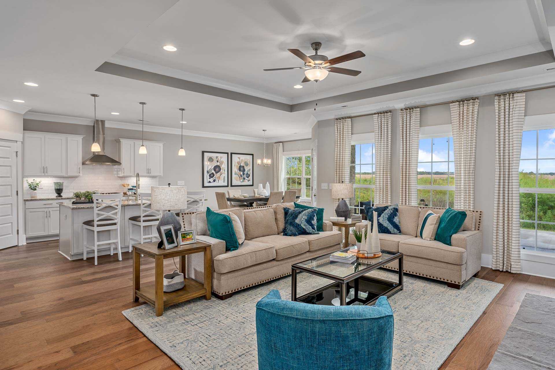 Open-concept living room in Kendall Downs Toney AL with hardwood floors beige sofa teal accents modern kitchen island and large windows