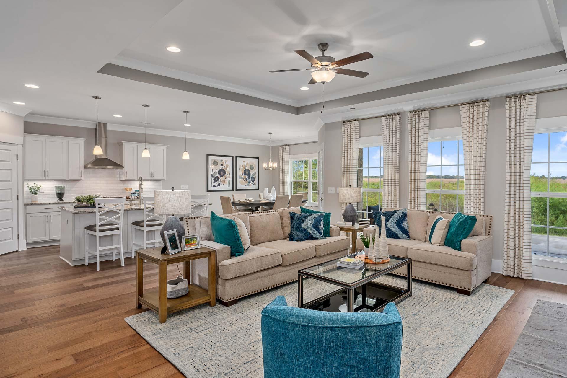 Open-concept living room in Kendall Downs Toney AL with hardwood floors beige sofa teal accents modern kitchen island and large windows