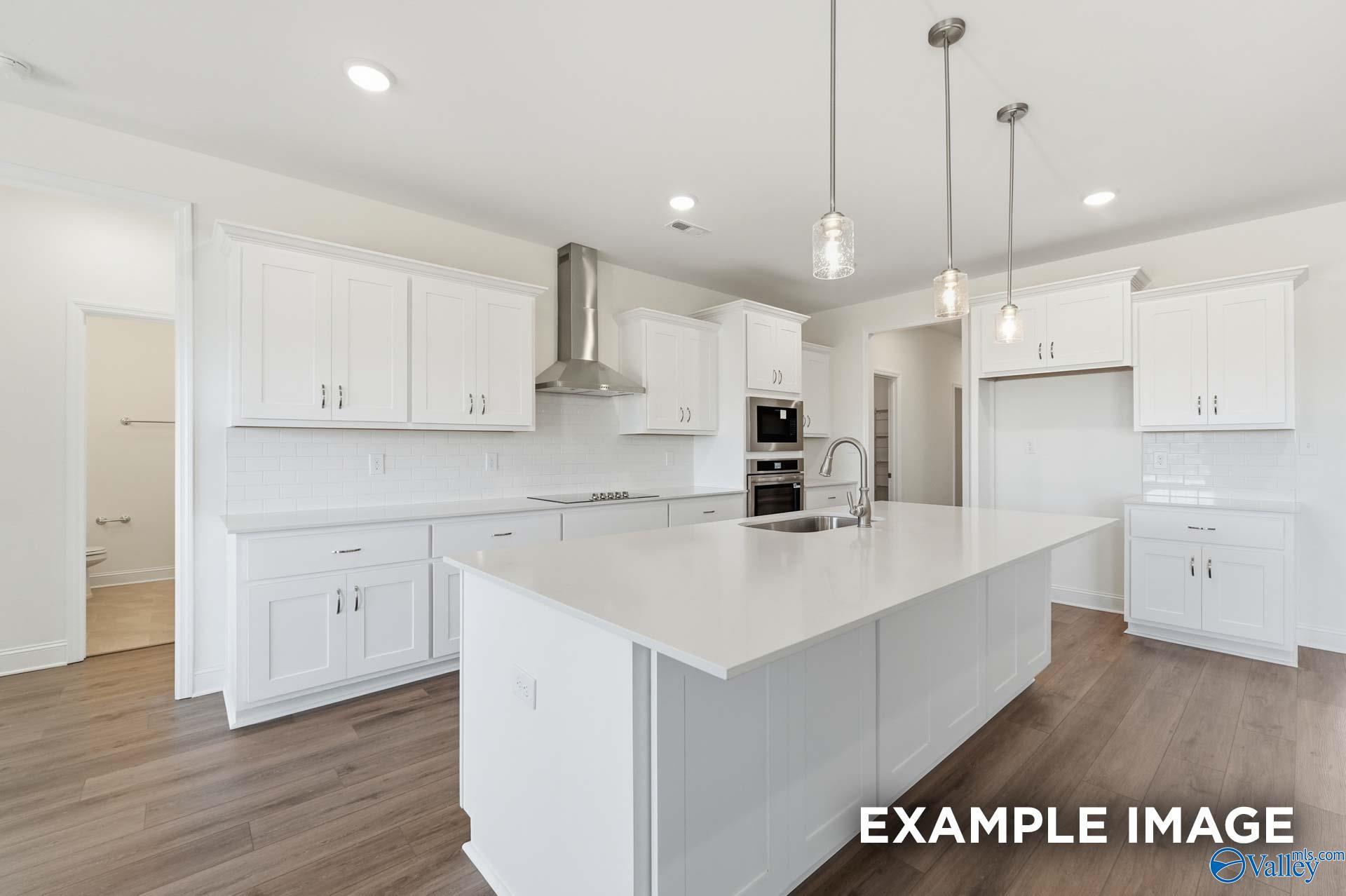 Modern white kitchen with quartz island, stainless steel appliances, and pendant lighting in The Valencia, Briercreek.