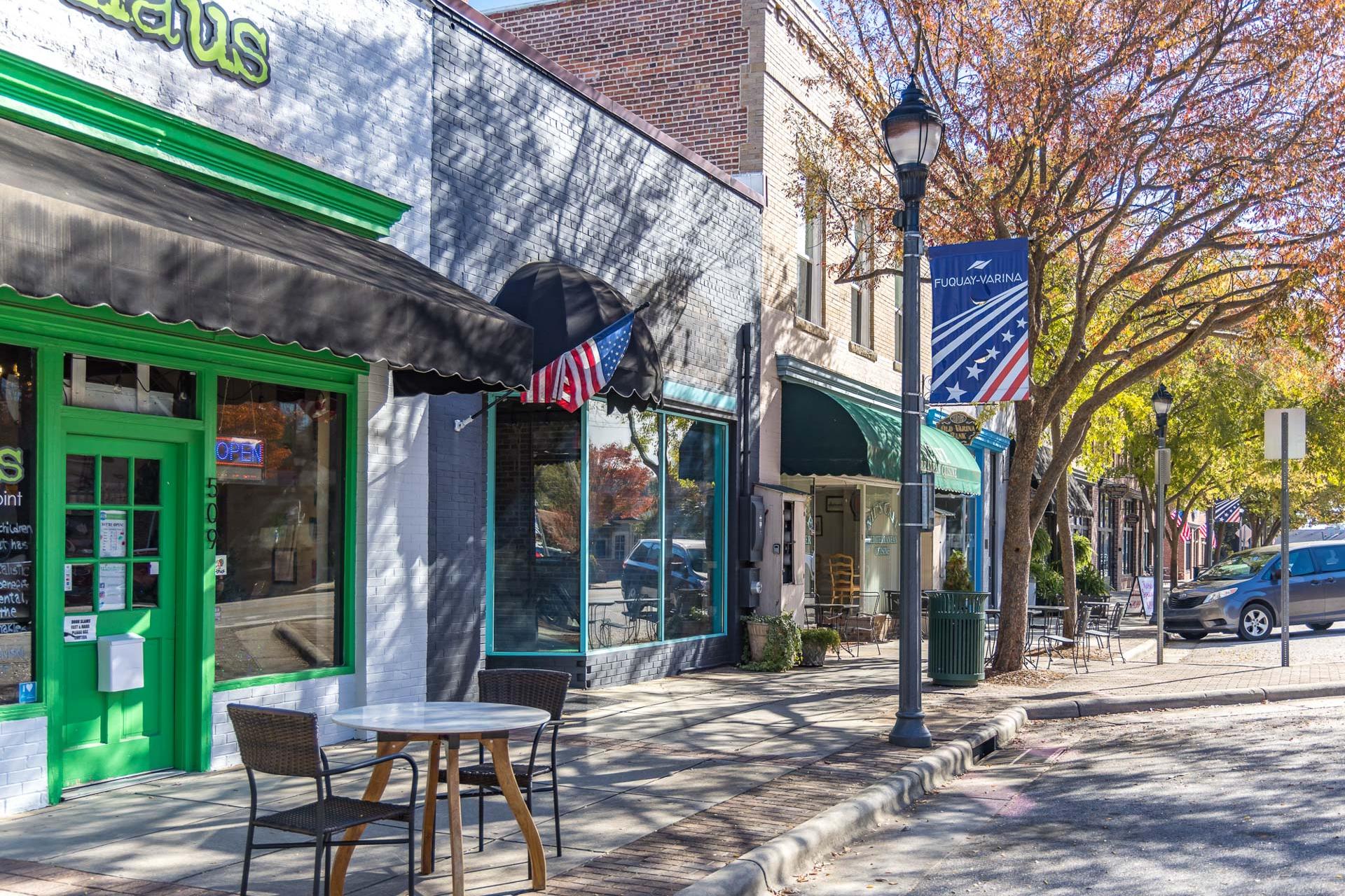 Quaint Fuquay-Varina street with green awning shops, American flags, outdoor cafe tables, and autumn trees near Prince Place NC