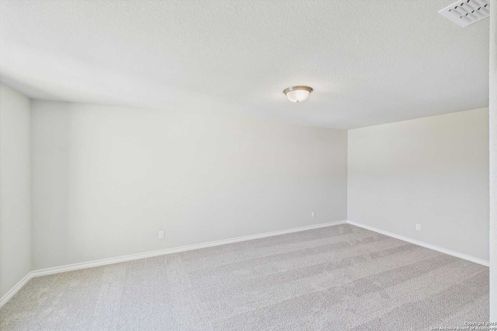 Spacious empty bedroom with neutral beige walls, carpeted floor, and ceiling light in Davidson Homes The Jennings H, Ladera, San Antonio