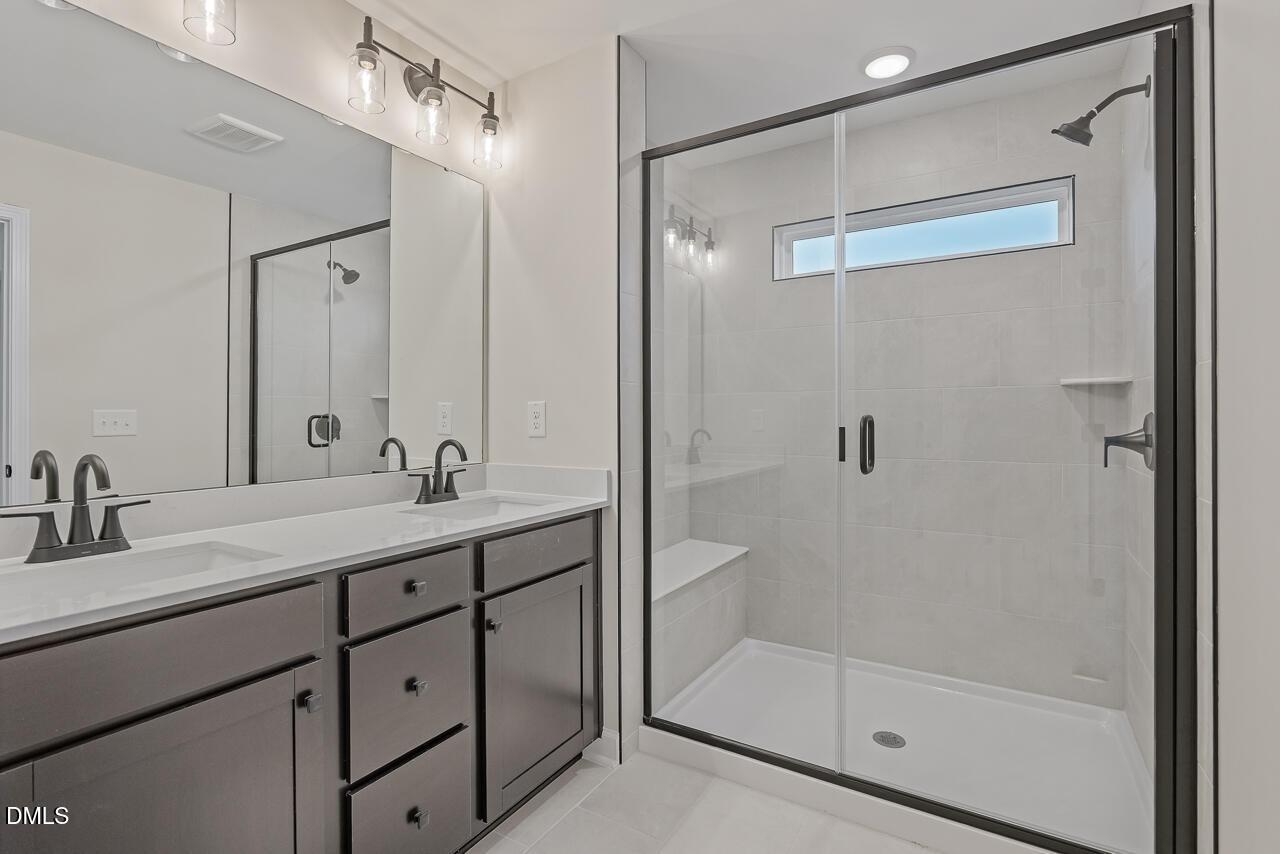 Modern master bathroom featuring double vanity, quartz counters, dark cabinets, and frameless glass shower in Davidson Homes The Mitchell, Knightdale, NC