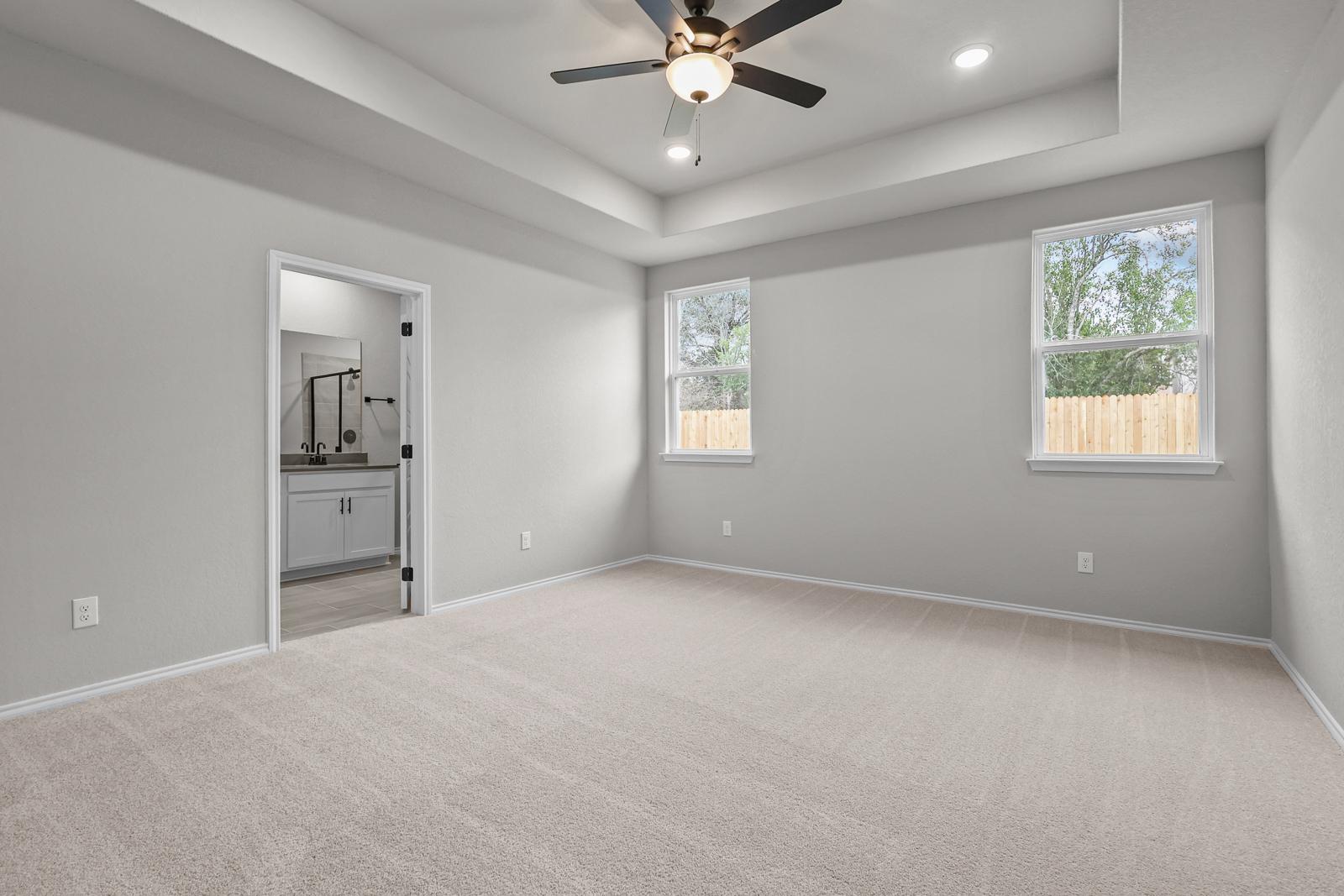 Spacious master suite with tray ceiling, carpeted flooring, and ensuite bathroom in The Glenwood by Davidson Homes.