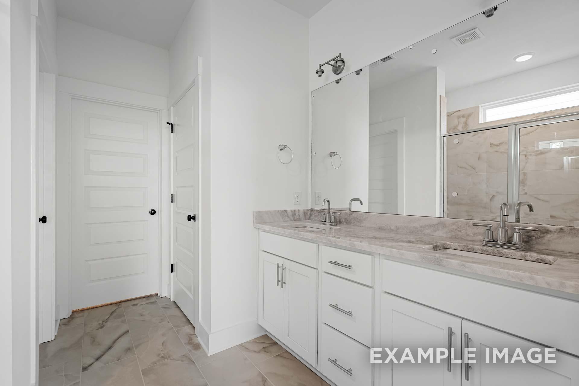Spacious master bathroom in The Ash plan with double vanity, quartz counters, large mirror, and glass shower enclosure