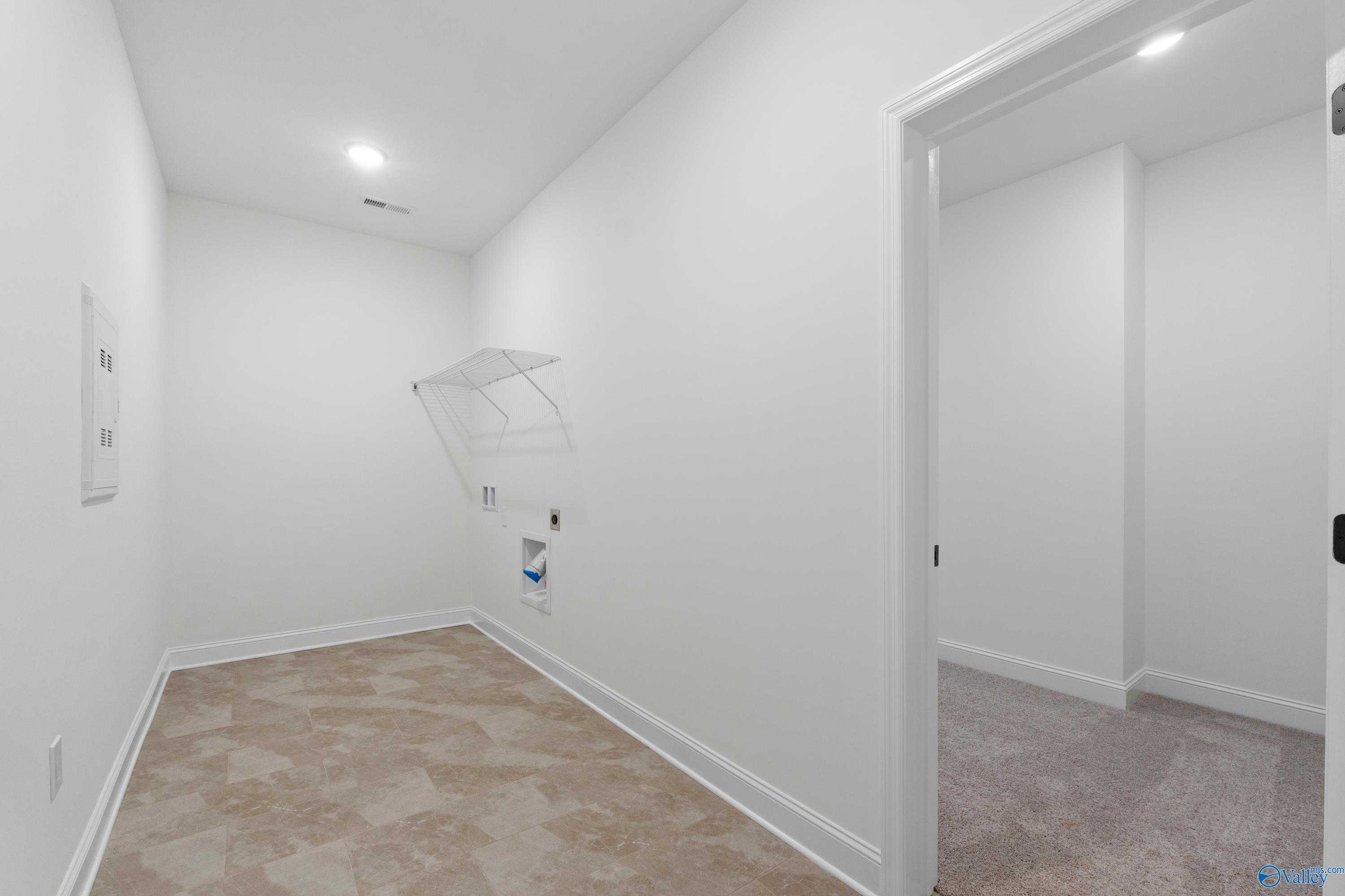 Bright laundry room with washer-dryer hookups and hanging rod in The Rockford B by Davidson Homes, Kendall Farms, Toney, Alabama