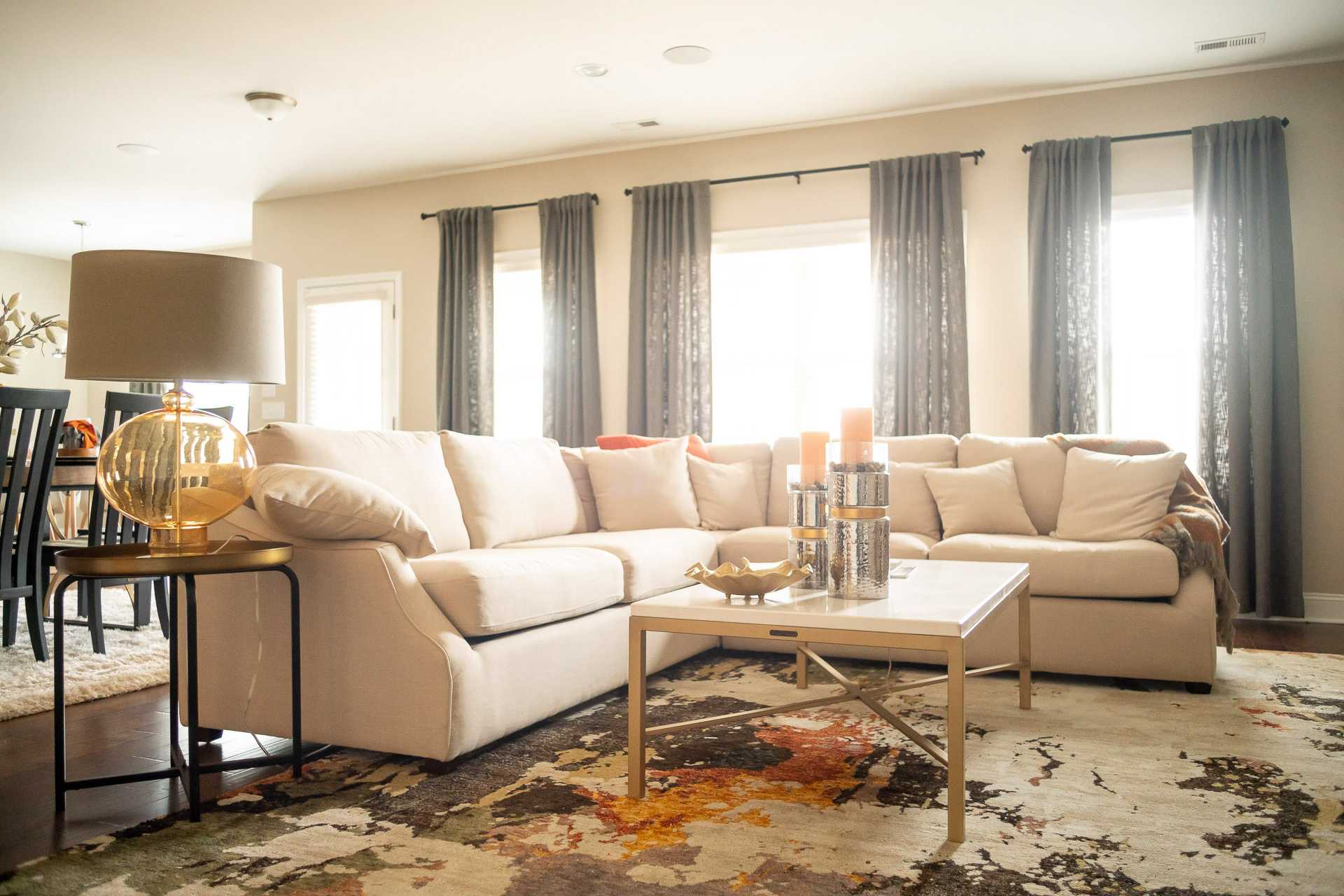 Spacious living room in Summer Pointe Madison AL with beige sectional sofa, metallic coffee table, candles, and large curtained windows