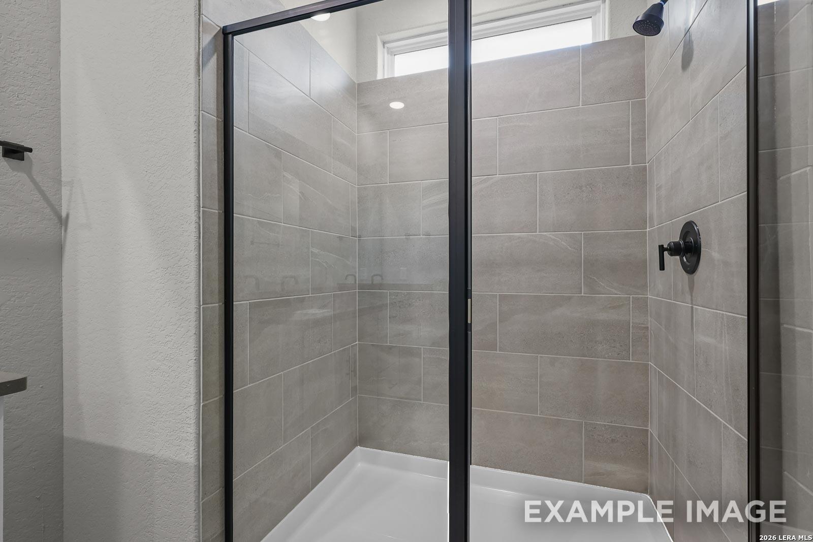Modern walk-in shower with neutral tile and black fixtures in a Glenwood E floor plan home in Royal Crest, San Antonio.