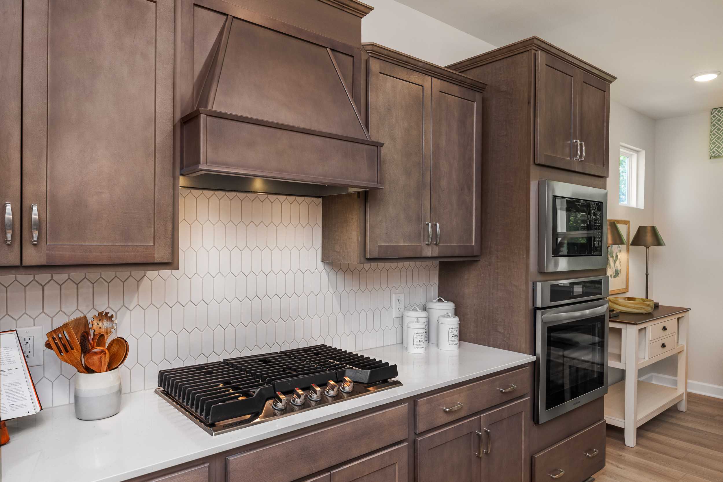 Modern kitchen with warm shaker cabinets, white hexagonal backsplash, gas cooktop and double ovens at Retreat at North Main, Lillington NC