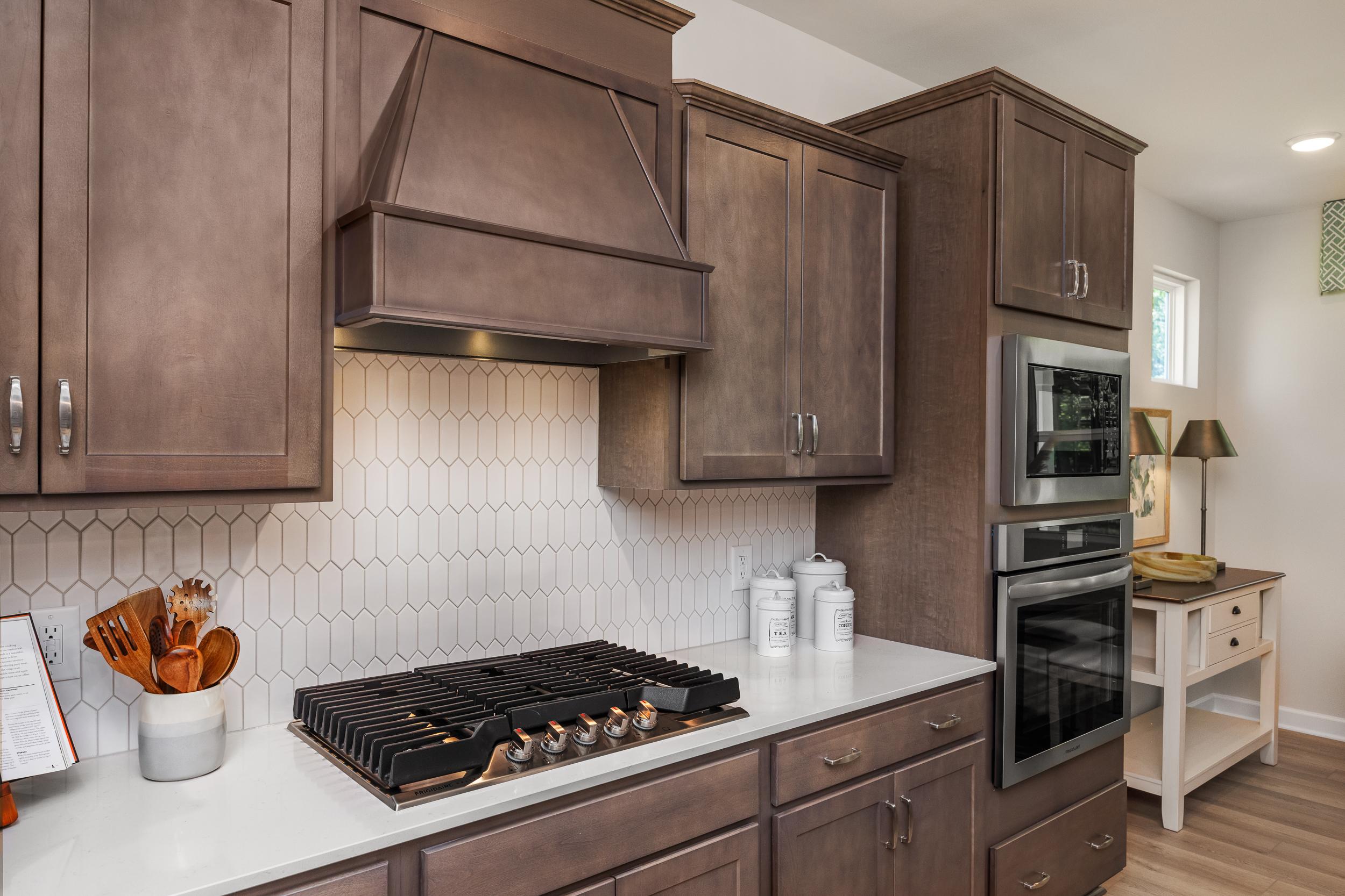 Modern kitchen with warm shaker cabinets, white hexagonal backsplash, gas cooktop and double ovens at Retreat at North Main, Lillington NC
