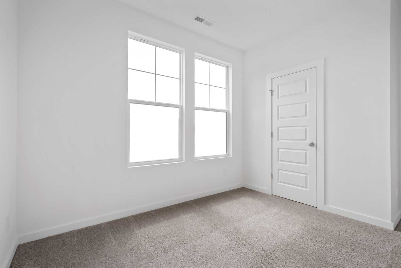 Spacious master bedroom in The Asheville with large grid windows, white door, and neutral carpet flooring