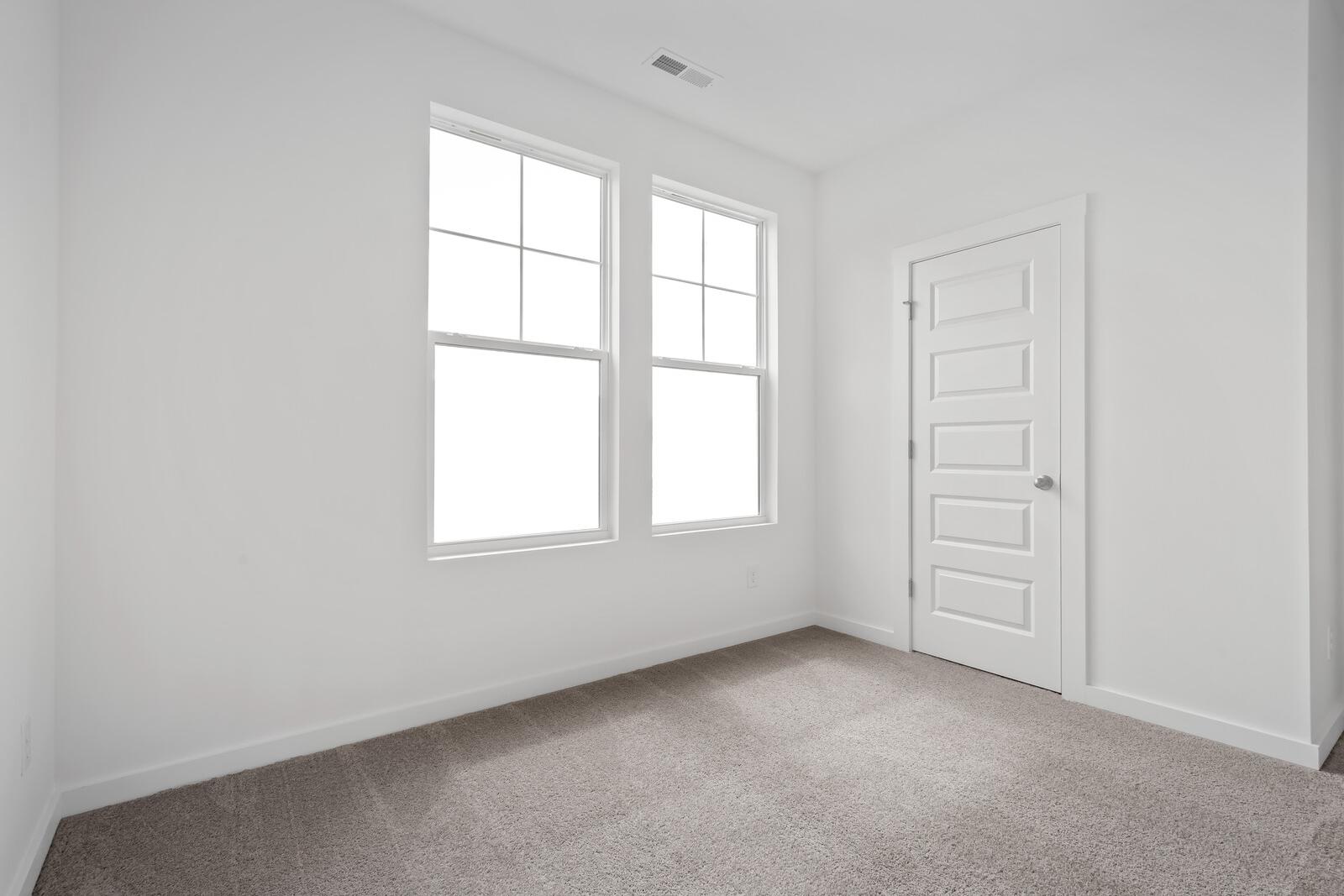 Bright empty bedroom in The Asheville Davidson Homes design featuring large grid windows and neutral carpet