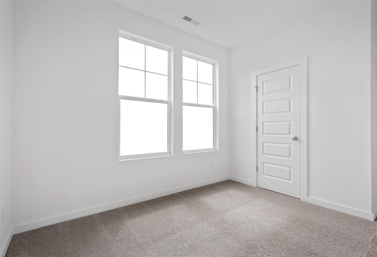 Bright empty bedroom in The Asheville Davidson Homes design featuring large grid windows and neutral carpet