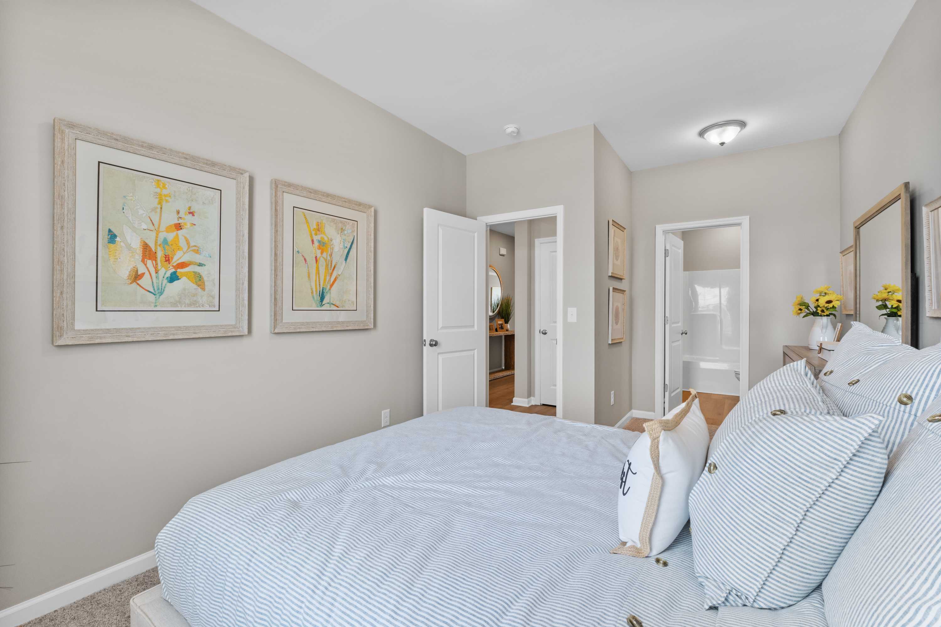Cozy bedroom at Anderson Farm in Athens Alabama with blue striped bedding, yellow floral art, and en-suite bath door