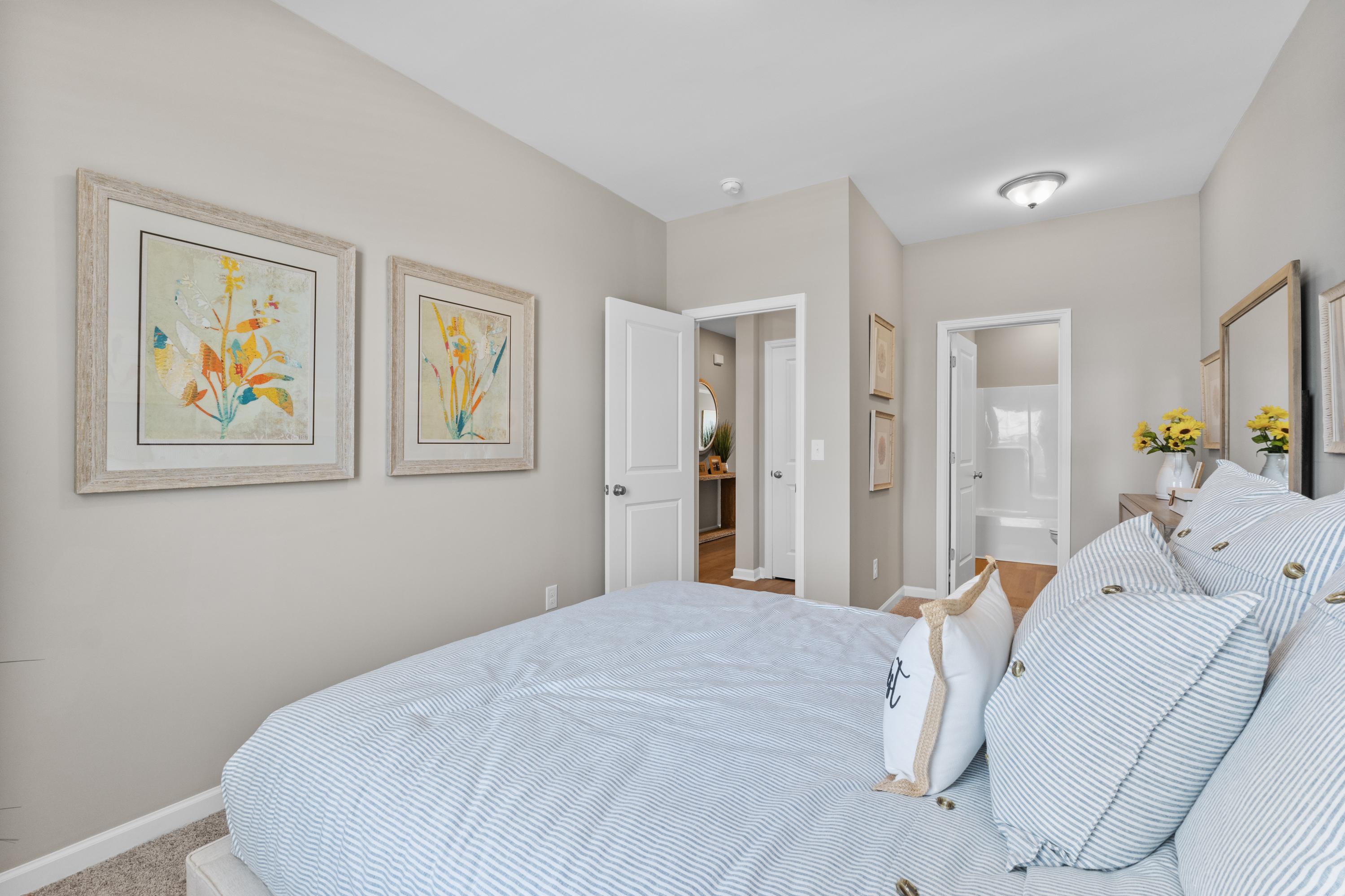 Cozy bedroom at Anderson Farm in Athens Alabama with blue striped bedding, yellow floral art, and en-suite bath door
