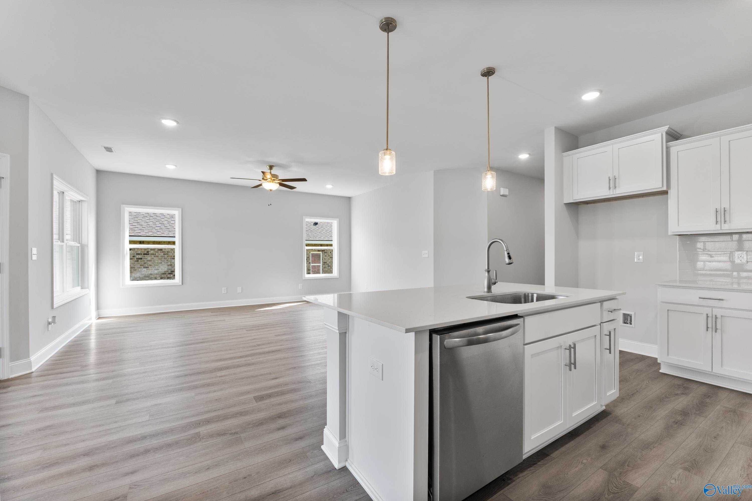 Modern open-concept kitchen with white cabinets, stainless dishwasher, pendant lights, and island in Davidson Homes The Franklin C, Toney, Alabama