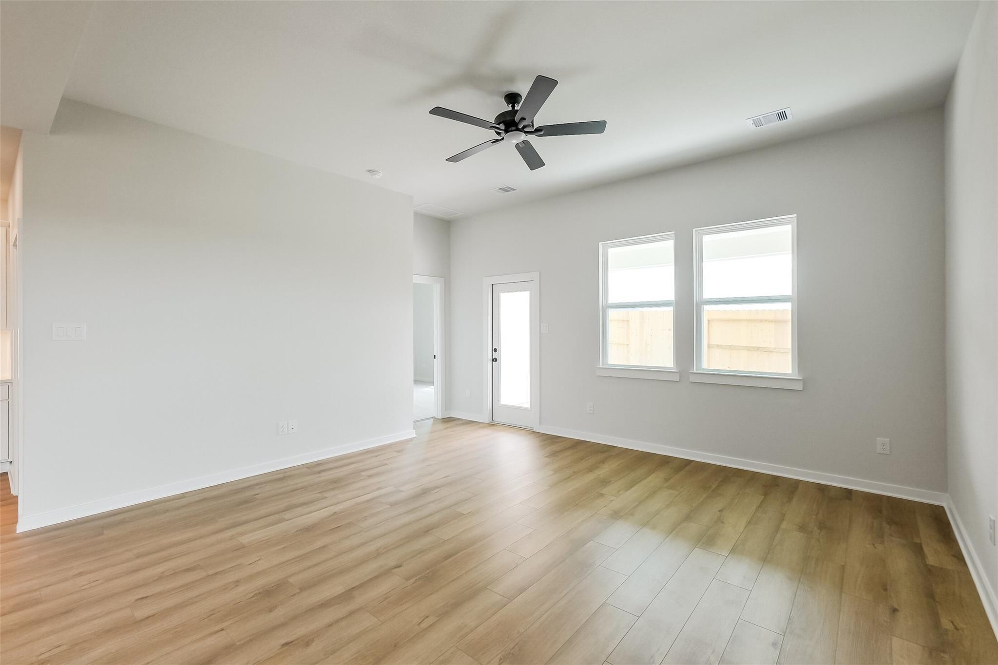 Bright living room with ceiling fan, double windows, French door, and hardwood floors in Davidson Homes The Tierra B, Beasley Texas