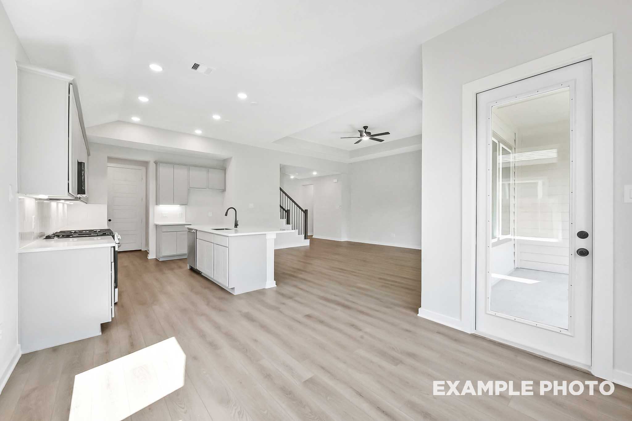 Open-concept kitchen and living area in The Sequoia home featuring white cabinets, large island, hardwood floors, ceiling fan