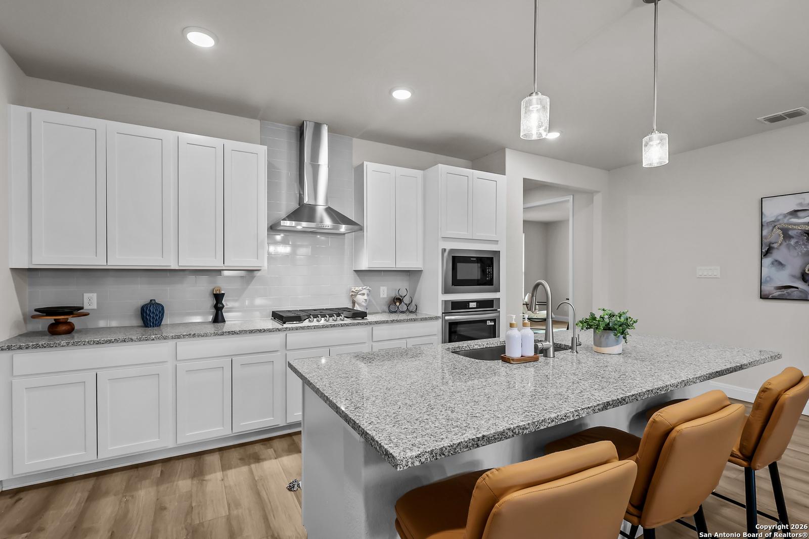 Modern kitchen featuring white shaker cabinets, granite island with orange bar stools, stainless steel appliances in Davidson Homes The Lanier H, Ladera San Antonio