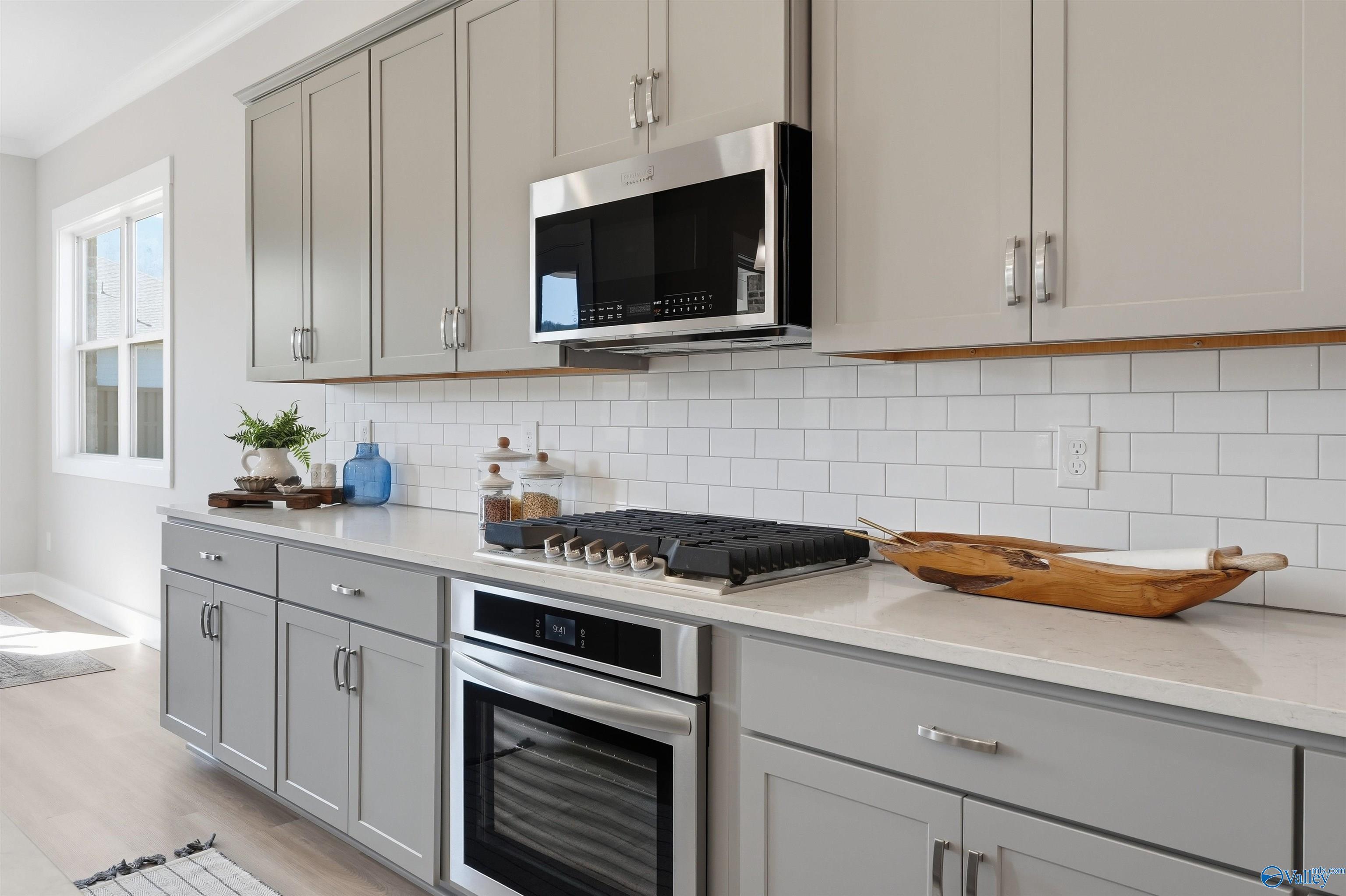 Modern kitchen with gray shaker cabinets, white subway tile backsplash, quartz counters, stainless gas cooktop in Evermore Homes Oxford B, Owens Cross Roads