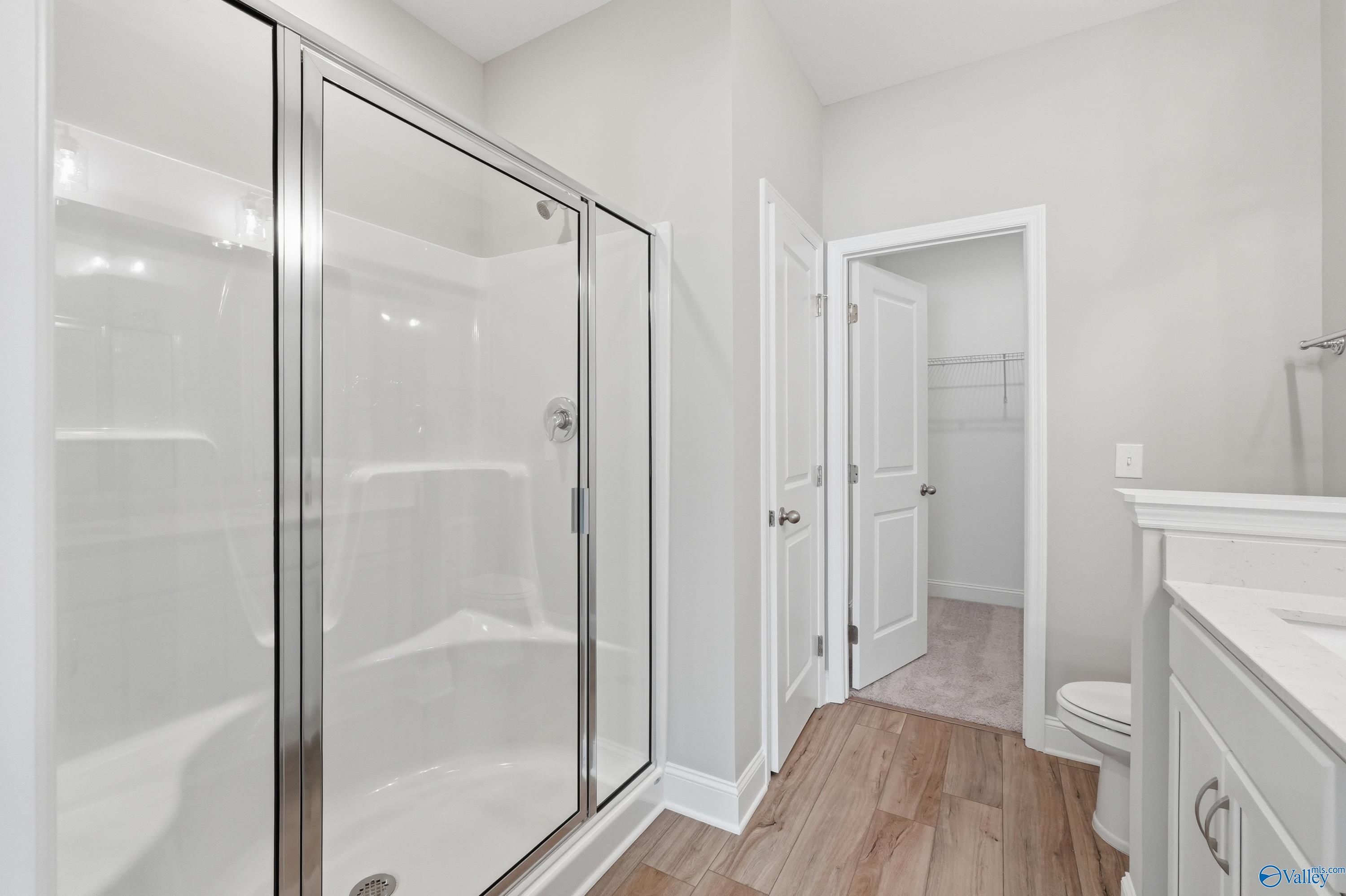 Modern master bathroom with frameless glass shower, white vanity sink, and wood floors in Davidson Homes The Asheville, Huntsville AL