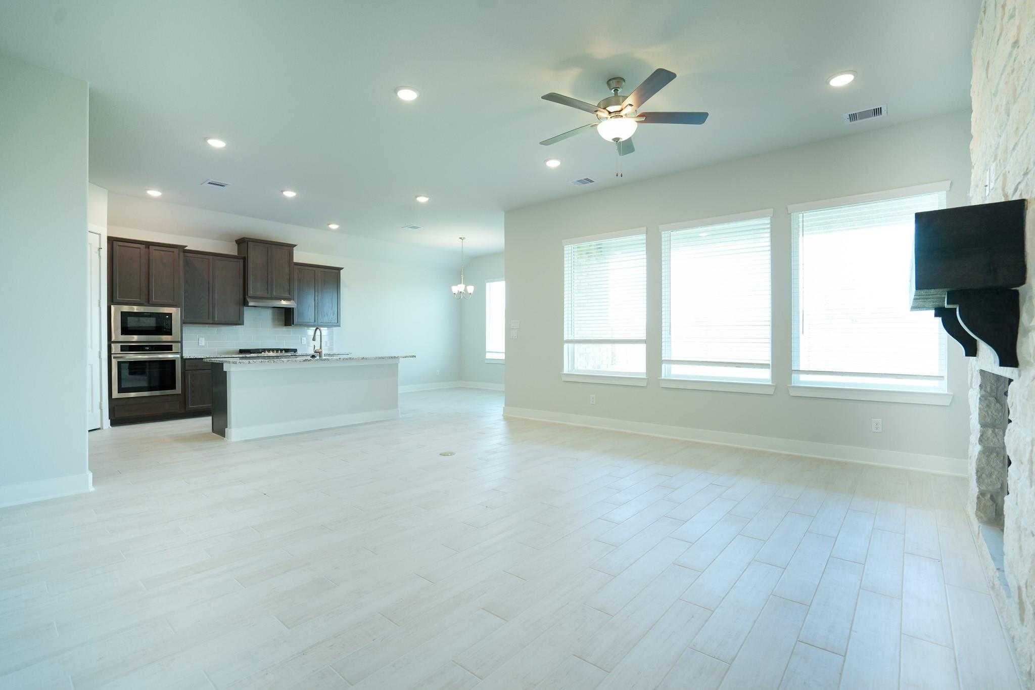 Open-concept kitchen-living area with dark cabinets, double ovens, island, large windows, and stone wall in Davidson Homes The Edward C, Lago Mar